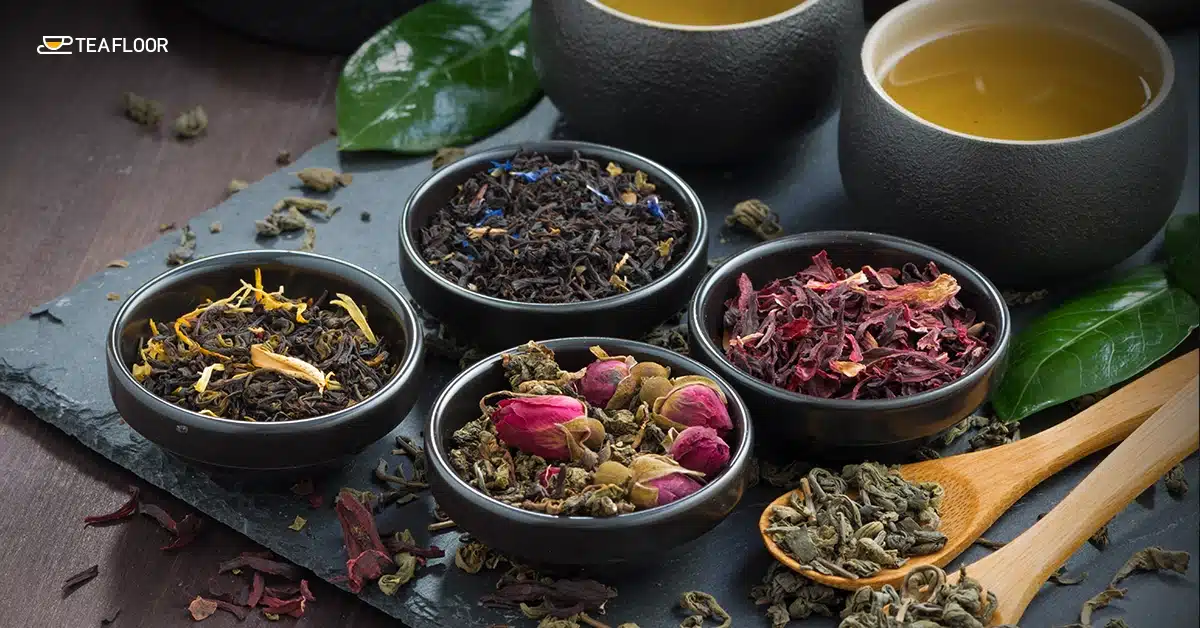 A top view of various colorful dry herbs and ingredients arranged neatly in small wooden spoons and ceramic bowls on a dark rustic surface